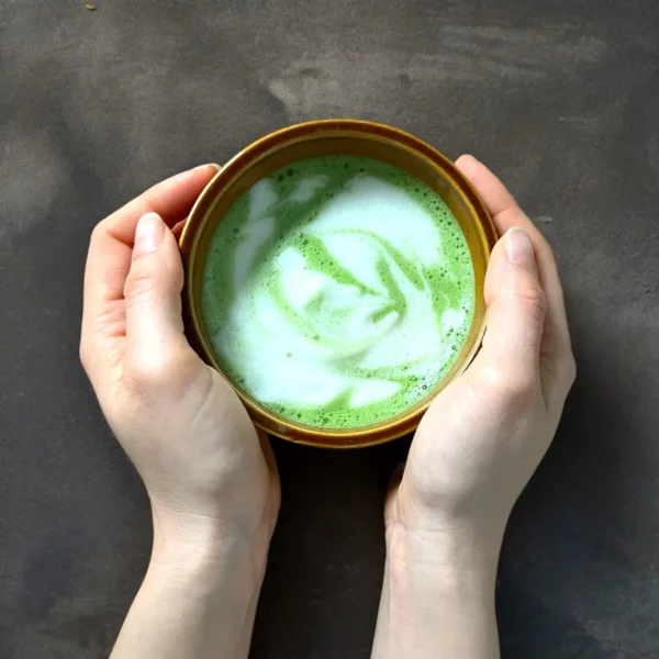 Bol de thé matcha avec mousse onctueuse tenu dans les mains